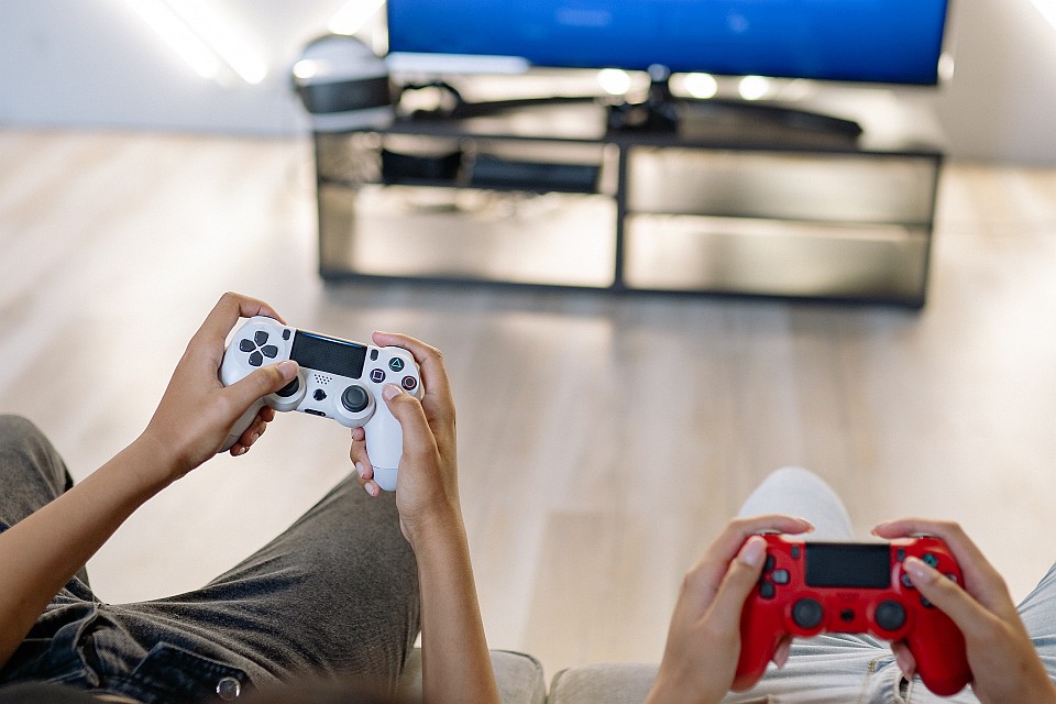 Two pairs of hands, both holding a gamepad. TV on the background.