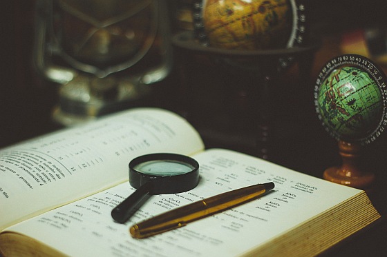 Photograph of an open book with a magnifying glass and a pen on top.