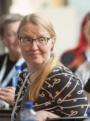 Seminaariin osallistuva henkilö istuu yleisössä ja katsoo sivulle. Taustalla näkyy muita tapahtuman osallistujia.